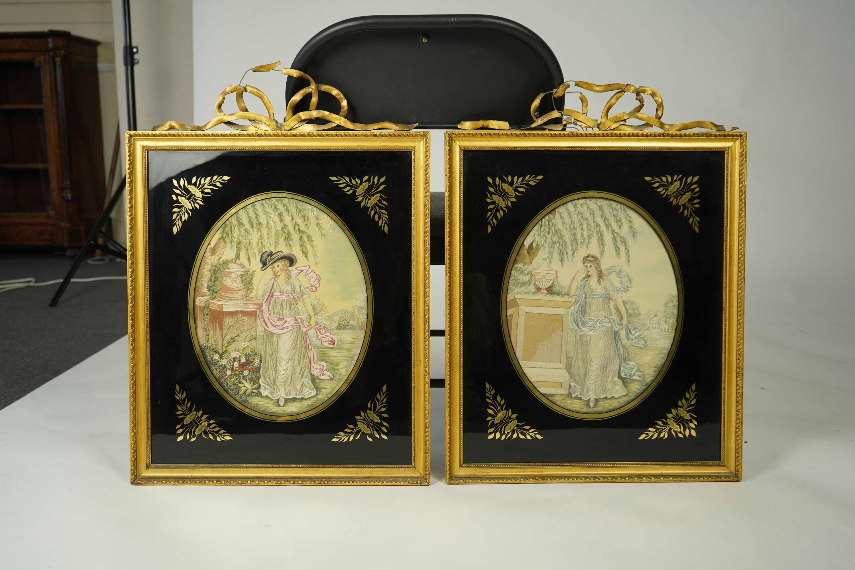 A pair of early 20th century oval silk embroideries of ladies standing by classical stone urns in a garden. Worked in pastel shades in silk using mostly stem stitch. Their faces, arms, hands and back ground silk hand pai